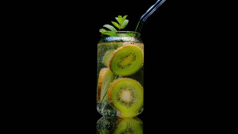 Detox drink made from fresh kiwi in sparkling water with mint in glass jar with straw rotating on black background. Mojito fruit cocktail.