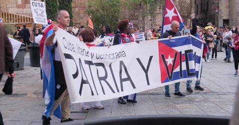 Barcelona, Spain - 2 November 2021: Cubans walk with political posters about Cuba politics and slogans across Barcelona with Cuban flag