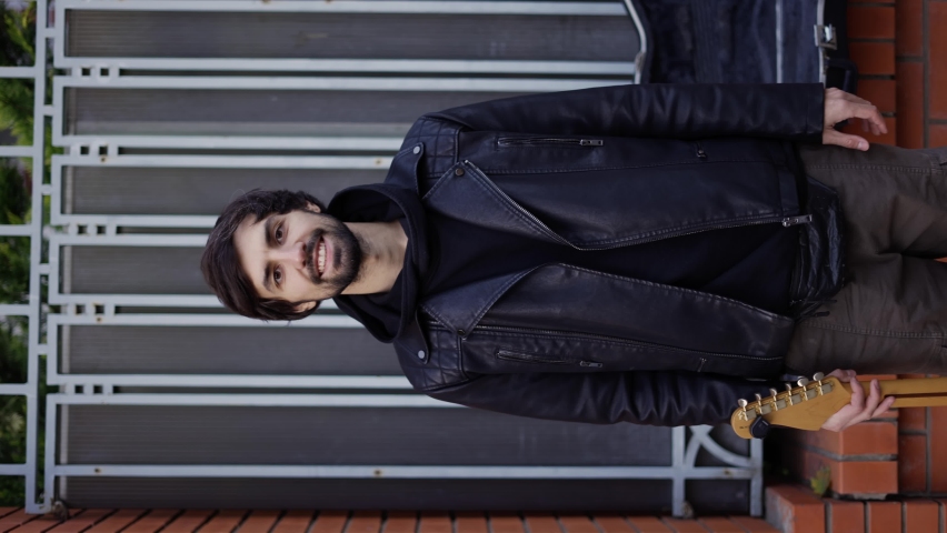 Man smiling on the street and carrying a guitar