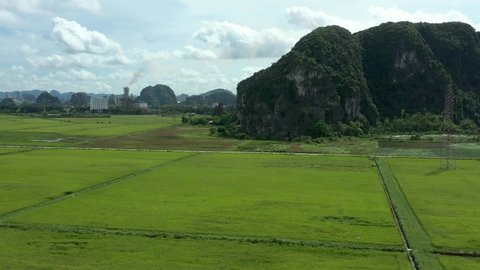 aerial drone shot of rice field mountains and big factory on background throwing pollution in the air. Ninh Binh province, Vietnam. 