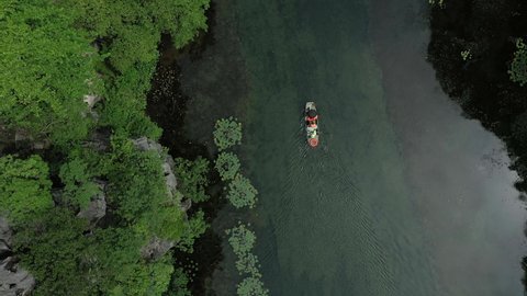 aerial drone shot of floating boat with passenger tourists in the middle of the river between mountains in Ninh Binh National park, Vietnam. Flying above, bird view.