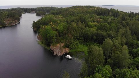 Motorboat anchored at quiet corner of Murolahti bay, aerial shot. Green forested rocks around, Ladoga lake seen at distance, scenic Republic of Karelia nature. Warm and quiet weather at summer day