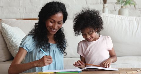Young African mother and cute little 5s daughter drawing together with colored pencils in sketchbook at home, loving family spend free time activities, enjoy creative hobby, child development concept
