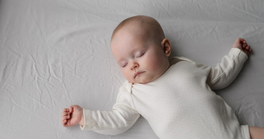 Sleeping like a newborn. Healthy happy little infant relax on big cozy bed nap alone spreading tiny hands wide. Cute funny baby dreaming well in comfy clothes enjoy safety comfort silence at bedroom Royalty-Free Stock Footage #1083762274