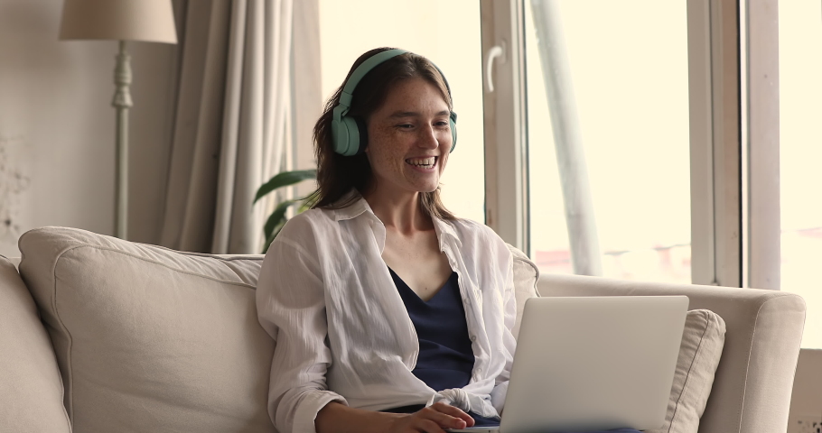 Young 20s freckled woman sit on sofa with laptop wear headphones take part in video conference by study or work, participate in streaming communication. On-line counselling event, modern tech concept Royalty-Free Stock Footage #1083762394