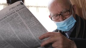 Old grandfather reads a newspaper sitting in a cafe.