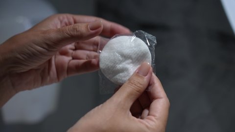 Closeup view 4k video footage of one soft cotton pad in hands of woman standing in bathroom. Guest of turkish hotel unpacking new pack with cotton swab 