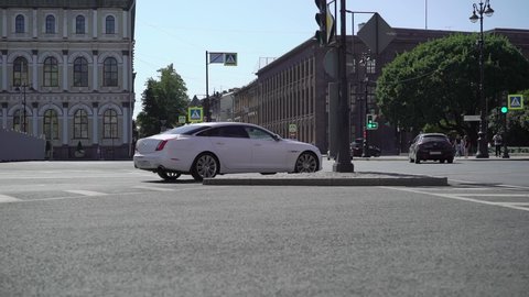 SAINT-PETERSBURG, RUSSIA - JULY, 17, 2021: White luxury sedan Jaguar XJ long car driving at summer city road. Auto on a street, crossing intersection.