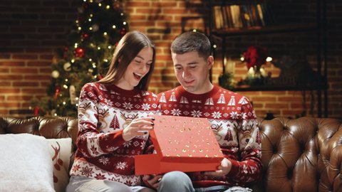 Woman is surprised and excited after opening received gift box. Happy man is making christmas gift to his beloved woman. Concept of holidays, romance, surprise. Holiday miracle