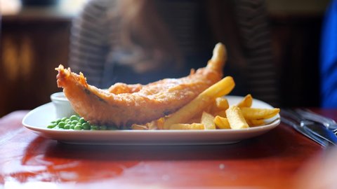Steaming plate of battered fish and chips with a side of green peas