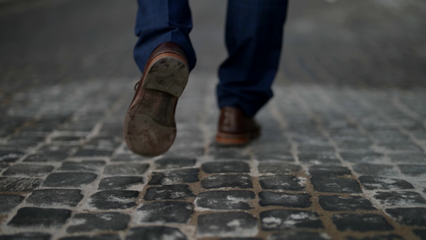 elegant man is walking over paving stones road in old city, closeup of feet