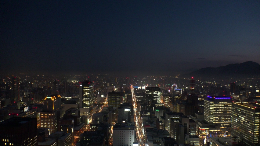 SAPPORO, HOKKAIDO, JAPAN - FEB 2020 : Aerial high angle wide view of cityscape of Sapporo city at night. View of street traffic and buildings around Susukino downtown area.