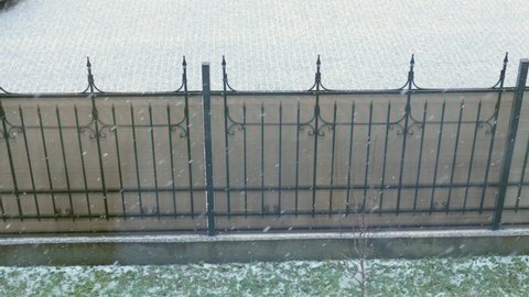first white snow falling outside, view from home window, snowflakes on green grass, brown fence and clear road. 