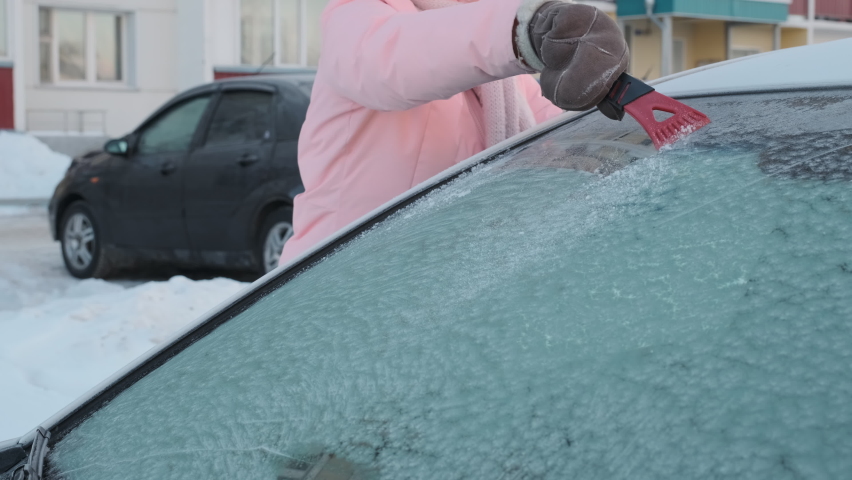 Woman is Cleaning a Windshield of her Car with Ice Scraper, Winter Driving