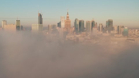 Amazing shot of downtown panorama coming out from dense fog. Group of high rise buildings lit by morning sun. Warsaw, Poland