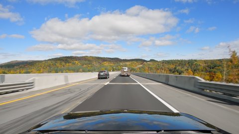 Driving a car on asphalt highway road in Vermont with multi color trees in fall season. Sunny day with blue sky