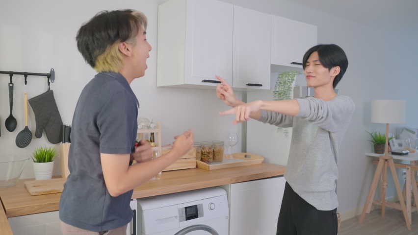 Asian happy handsome man gay couple sing and dance together in kitchen. Attractive romantic male lgbt couple wear apron, spending free leisure time and enjoy listen to music and cooking foods in house