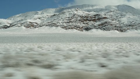 Road trip to Death Valley, driving auto, snow in California, USA. Hitchhiking winter traveling in America. Highway, mountain pass and dry barren wilderness. Passenger POV from car. Journey to Nevada.