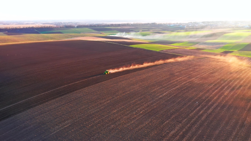 A cloud of dust rises behind a tractor plowing the ground from a bird's eye view. Spring soil preparation for sowing crops. Cinematic top down aerial shot. Ukraine, Europe. Filmed in 4k, drone video. Royalty-Free Stock Footage #1083789322