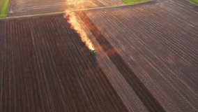 A cloud of dust rises behind a tractor plowing the ground from a bird's eye view. Spring soil preparation for sowing crops. Cinematic top down aerial shot. Ukraine, Europe. Filmed in 4k, drone video.