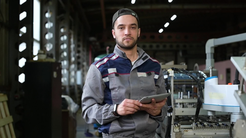 Portrait of a young worker of an assembly line at a factory for the production of various products. Young white man with tablet controls production processes