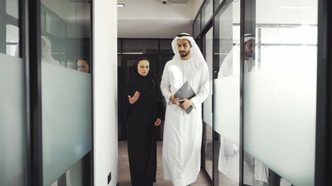 Man and woman with traditional clothes working in a business office of Dubai. Portraits of  successful entrepreneurs businessman and businesswoman in formal emirates outfits.