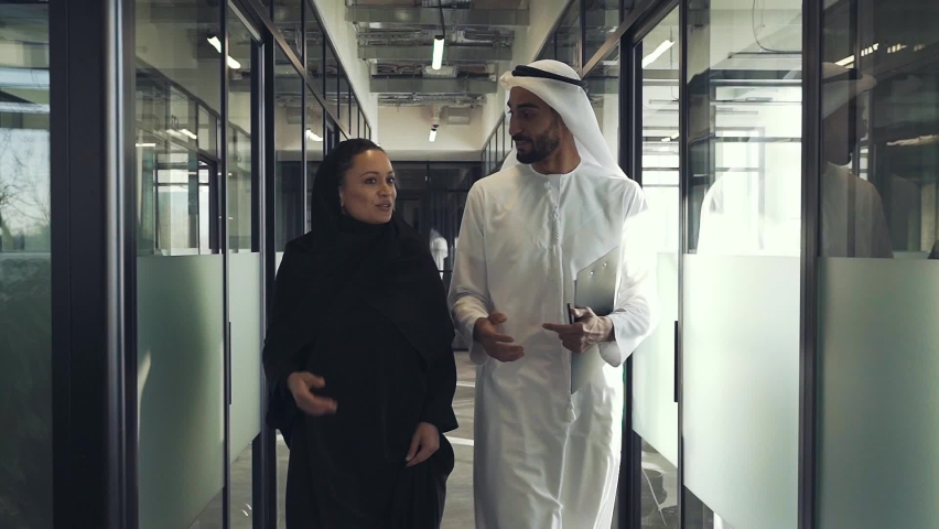 Man and woman with traditional clothes working in a business office of Dubai. Portraits of  successful entrepreneurs businessman and businesswoman in formal emirates outfits. Royalty-Free Stock Footage #1083797338