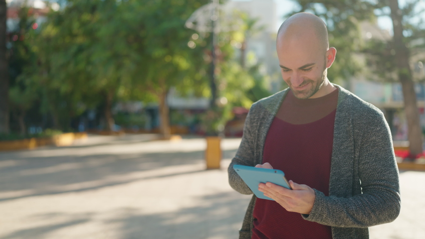 Young bald man smiling confident using touchpad at park