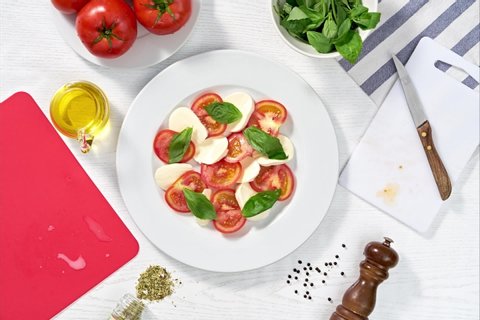 Stop motion preparation of a caprese salad with tomato, mozzarella, basil, oregano and virgin olive oil. Top view. Gourmet food concept.