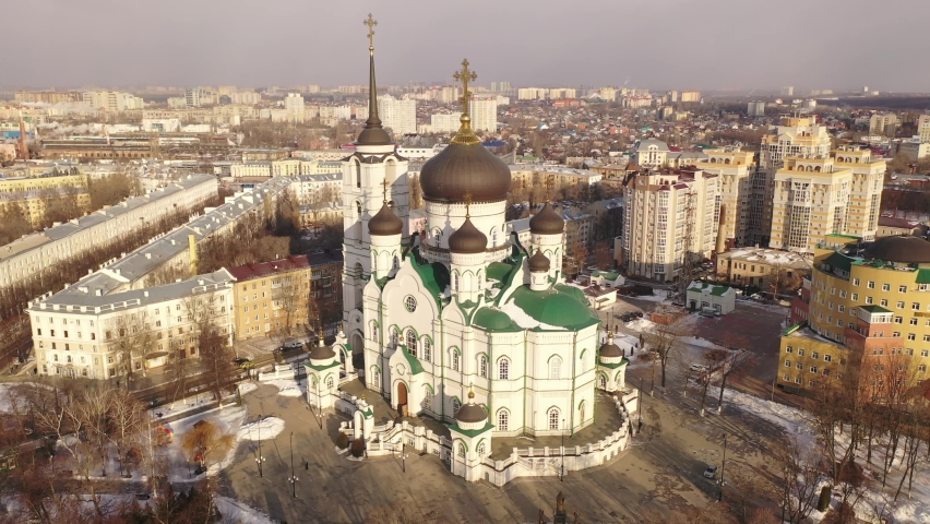 Aerial view of five-domed building of Annunciation Cathedral with attached bell tower in Voronezh on background with winter cityscape, Russia Royalty-Free Stock Footage #1083805579