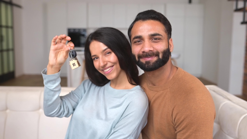 Happy Indian family couple showing new house keys to camera while posing Indoors. Own home, real estate ownership and housing. Mortgage and apartment purchase Royalty-Free Stock Footage #1083805714