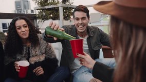 Caucasian male sitting, pouring a drink for his friends at a rooftop social gathering. Cheers with red cups. High quality 4k footage - Powered by Shutterstock - Get 15% off with code: PIKWIZARD15