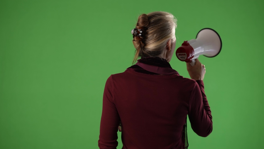 Mature blonde woman shouting into megaphone away from camera. Isolated on green screen chroma key.