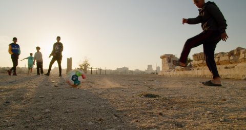 Amman, Jordan - NOVEMBER 24, 2021: Authentic Arab Teenager Boys Play Football on sunny Day at sunset. Eastern Kids and Children Play Soccer Game on Sand. 4K gimbal low angle wide shot in slow motion