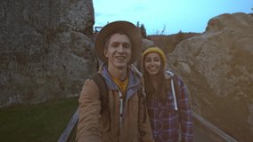 happy smiling couple hiker walks together in national park Tustan in Ukraine. man and woman making sefie on amazing landscape with spruces, rocks mountains and sunset sky on background.