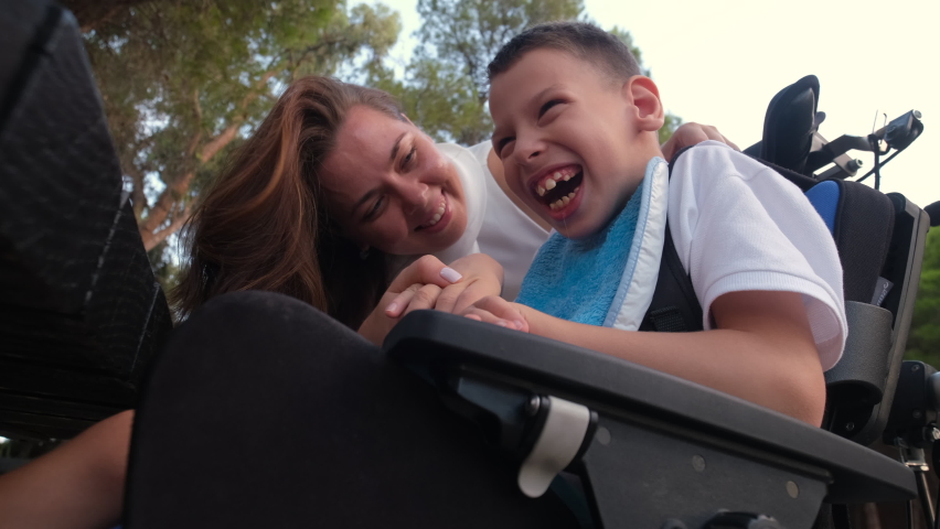 Loving mother feeling bond and love playing kissing on cheek her little 9s son sit in wheelchair outdoor Royalty-Free Stock Footage #1083819100