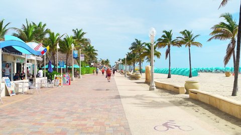 Hollywood, USA - August 4, 2021: Hollywood broadwalk boardwalk in Miami Beach Florida and people candid walking by restaurant riding bike on lane by ocean promenade