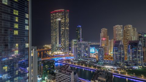 Dubai Marina skyscrapers and JBR district with luxury buildings and resorts aerial timelapse during all night with lights turning off. Illuminated waterfront and boats floating in canal