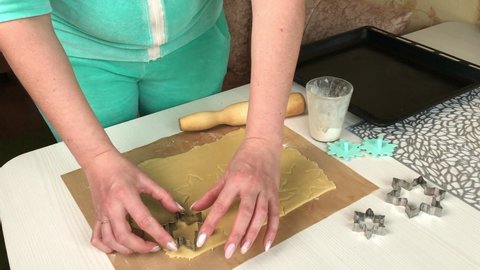 A woman squeezes cookies out of rolled out dough. With a snowflake shape. Cooking marshmallow sandwiches. The ingredients and tools are laid out on the table.