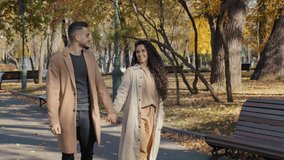 Young positive arabic couple walking holding hands date in autumn city park attractive girl happily whirling handsome bearded guy hugging girlfriend outdoors man and woman enjoying spend time together