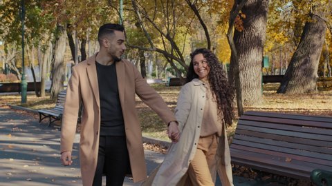 Young positive arabic couple walking holding hands date in autumn city park attractive girl happily whirling handsome bearded guy hugging girlfriend outdoors man and woman enjoying spend time together