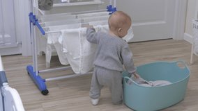 Cute little toddler child playing with clothes drying rack in living room, kid having fun exploring all around the house, 9 month old caucasian baby boy at home. High quality 4k footage