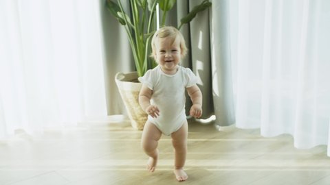 Happy Baby Girl Learning To Walk Toddler Taking First Steps Without Any Help, Walking On Warm Floor At Home, Baby first steps, Exploring Home, Child Smiling, Concept Newborn And Childhood, Slow Motion