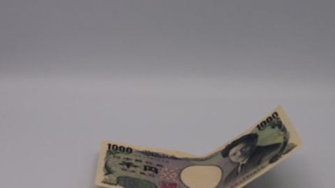 Japanese 1000-yen bill falling from above.
translation:Bank of Japan notes,Thousand yen,Bank of Japan,Manufactured by the National Printing Bureau,Hideyo Noguchi.