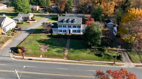 Large white house with shutters and dormer windows. Aerial establishing shot in autumn fall foliage.