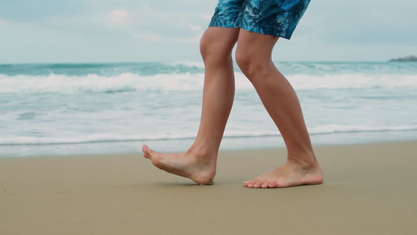 Unknown boy legs going backwards at sand beach. Barefoot teenager feet touching sand at seaside. Unrecognizable male person enjoying summer vacation at sea coastline. Royalty-Free Stock Footage #1083836038