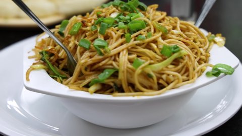 4K Closeup shot of Schezwan Sauce Noodles, Hakka Noodles, Chow Mein a popular Indian Chinese Fast Food dish, freshly prepared and served in a white bowl in a restaurant. Mumbai, Maharashtra, India.