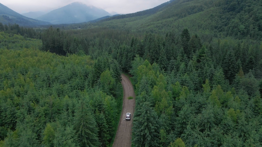 aerial view of suv car moving by path road in mountains overcast misty rainy weather tracking dolly shoot