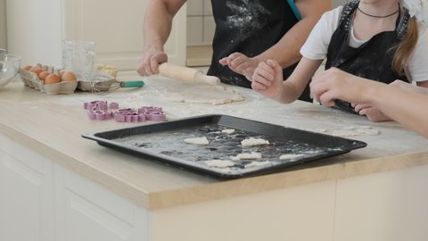 Family of Three Cooking Cookies Together at Home. Man in Kitchen Apron Rolling Out the Dough with a Rolling Pin while his Wife and Little Daughter Putting Raw Cookies on a Baking Sheet
