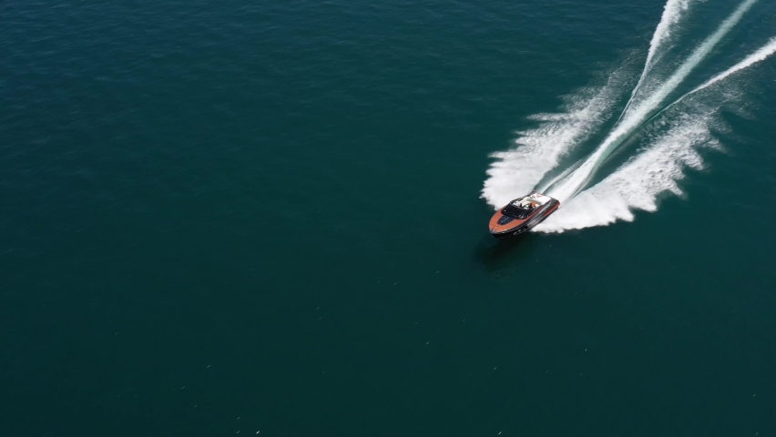 Luxury boat in dark color, fast movement on blue water, aerial view. Expensive luxury Italian boat moving on the water top view. Boat dark wood, movement on the water top view. Royalty-Free Stock Footage #1083842188